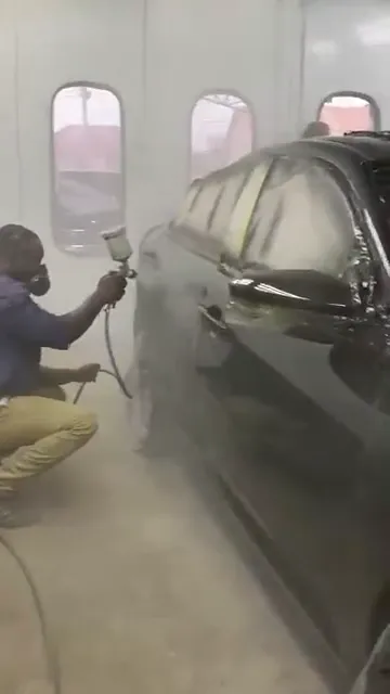Painter crouching to spray the side of the black Honda Civic in the spray booth